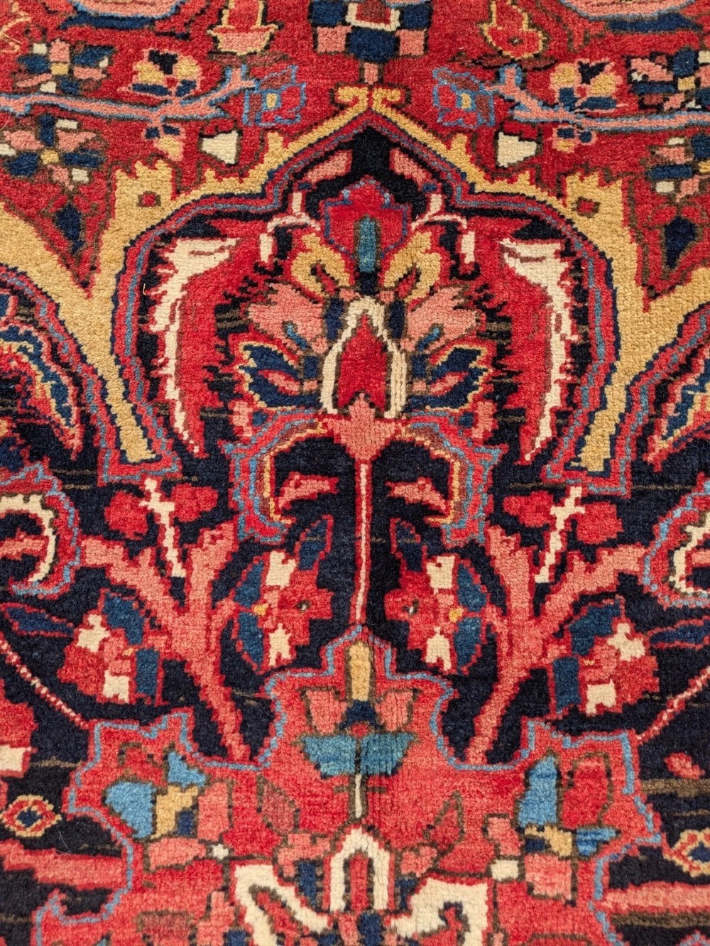 An antique hand-knotted Ahar Heriz wool carpet featuring a large central floral medallion surrounded by detailed vine motifs in rust red, navy blue, and ivory tones. View V
