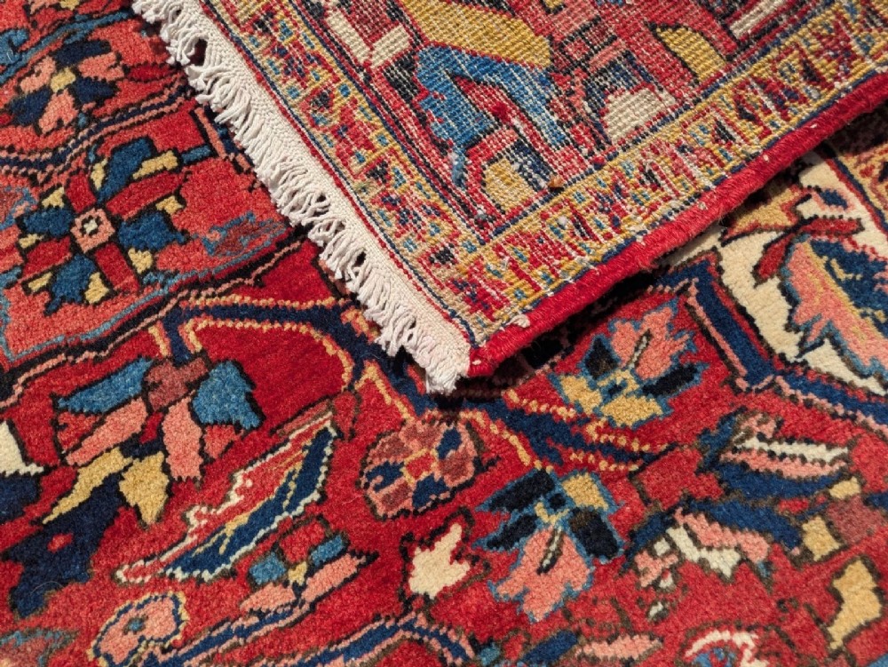 An antique hand-knotted Ahar Heriz wool carpet featuring a large central floral medallion surrounded by detailed vine motifs in rust red, navy blue, and ivory tones. View VI