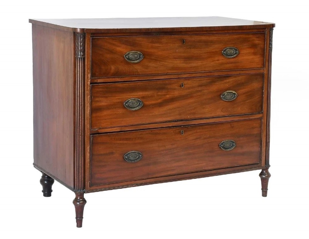 A George III mahogany chest of drawers featuring three full-width drawers with oval brass drop handles, reeded side columns, and turned feet.