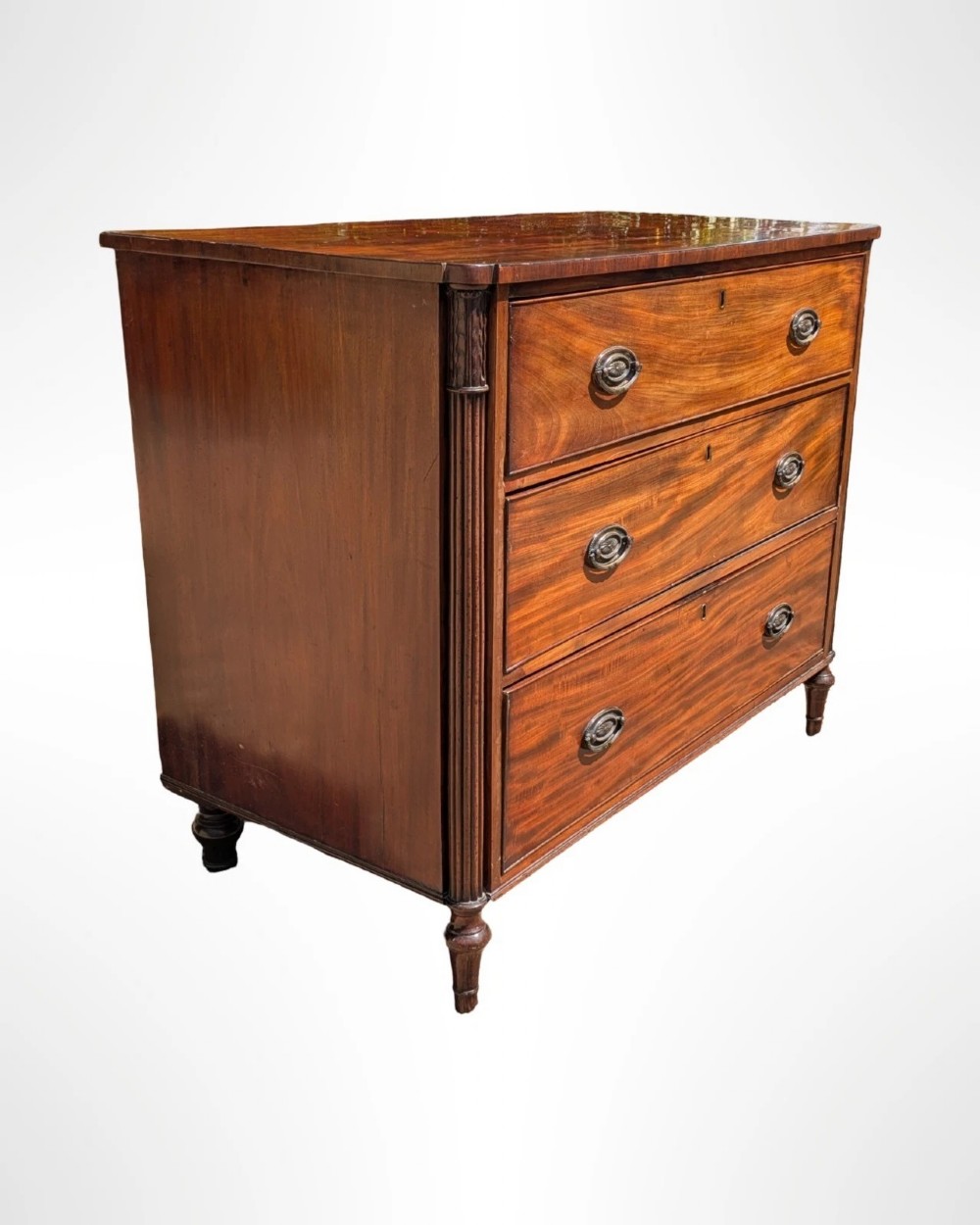 A George III mahogany chest of drawers featuring three full-width drawers with oval brass drop handles, reeded side columns, and turned feet. View III