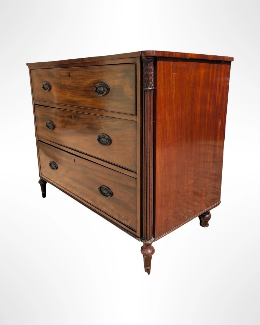 A George III mahogany chest of drawers featuring three full-width drawers with oval brass drop handles, reeded side columns, and turned feet. View IV