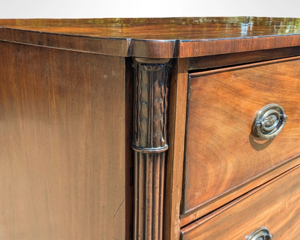 A George III mahogany chest of drawers featuring three full-width drawers with oval brass drop handles, reeded side columns, and turned feet. View V