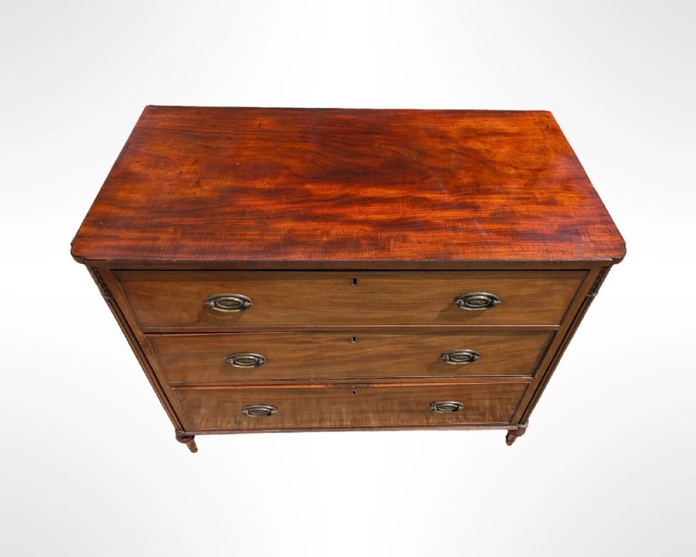 A George III mahogany chest of drawers featuring three full-width drawers with oval brass drop handles, reeded side columns, and turned feet. View VII
