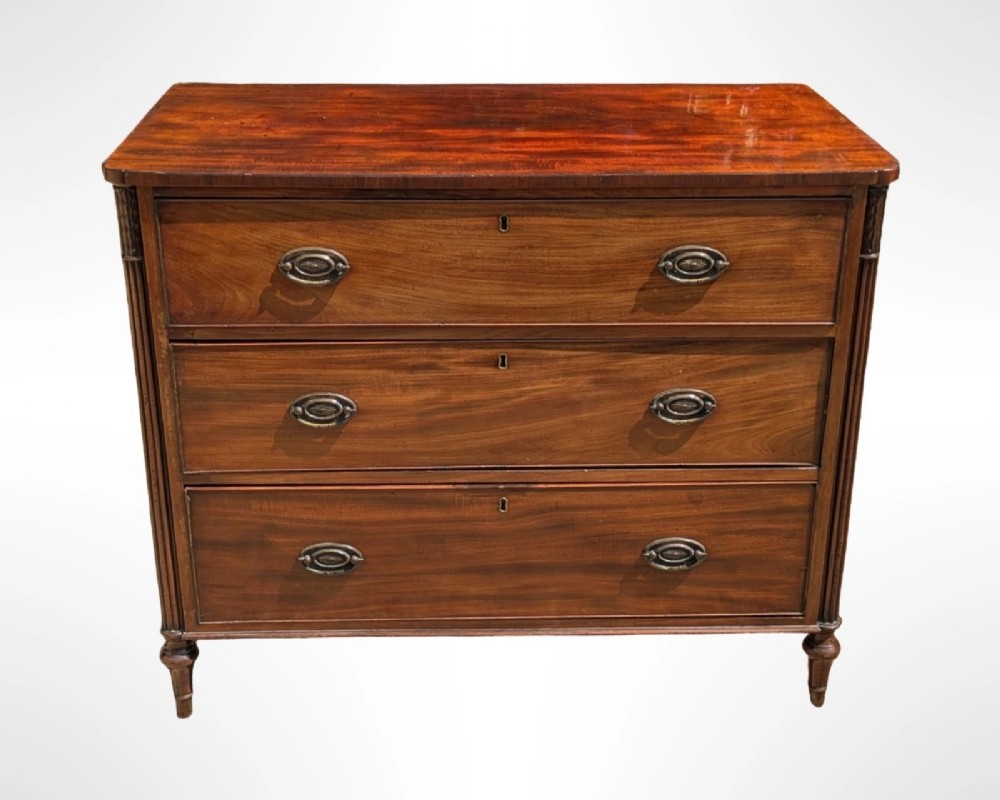 A George III mahogany chest of drawers featuring three full-width drawers with oval brass drop handles, reeded side columns, and turned feet. View VIII