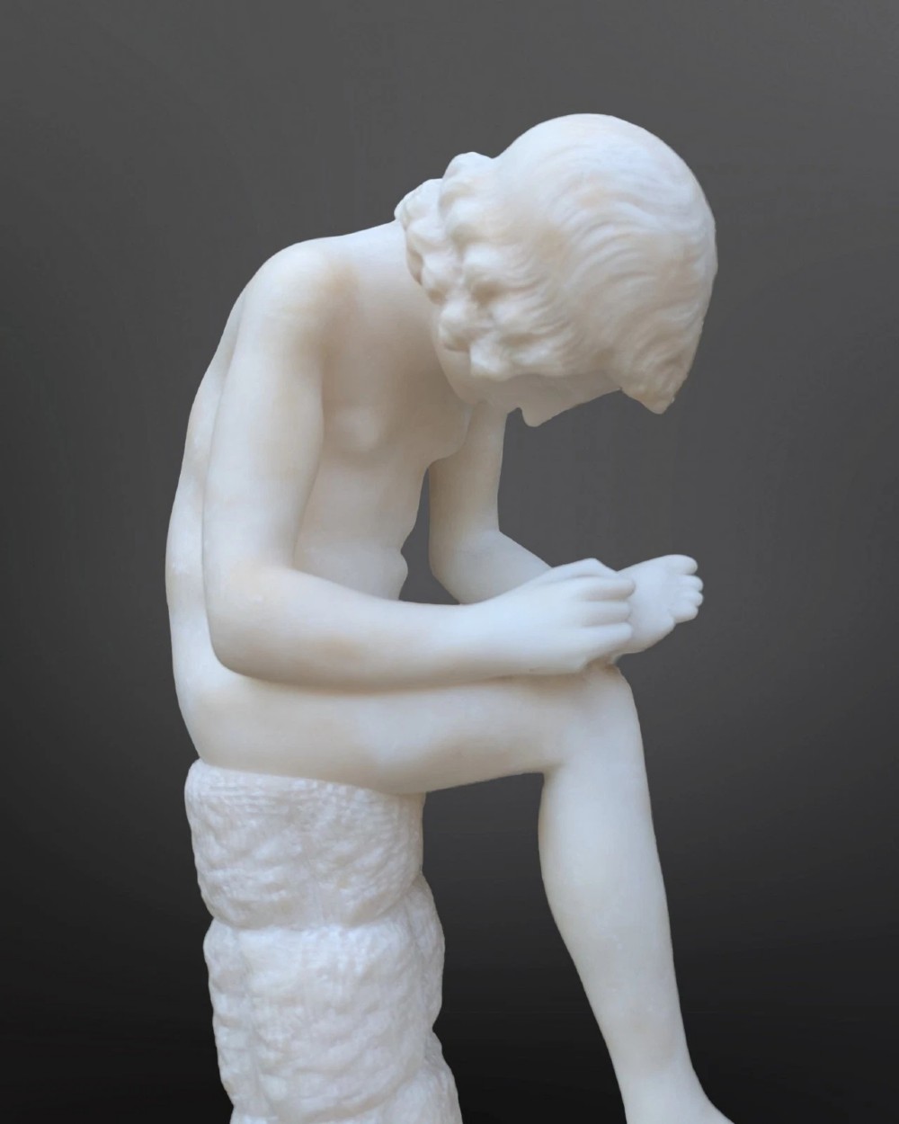 A carved white alabaster sculpture depicting a classical nude youth seated on a tree stump while extracting a thorn from his foot. View II
