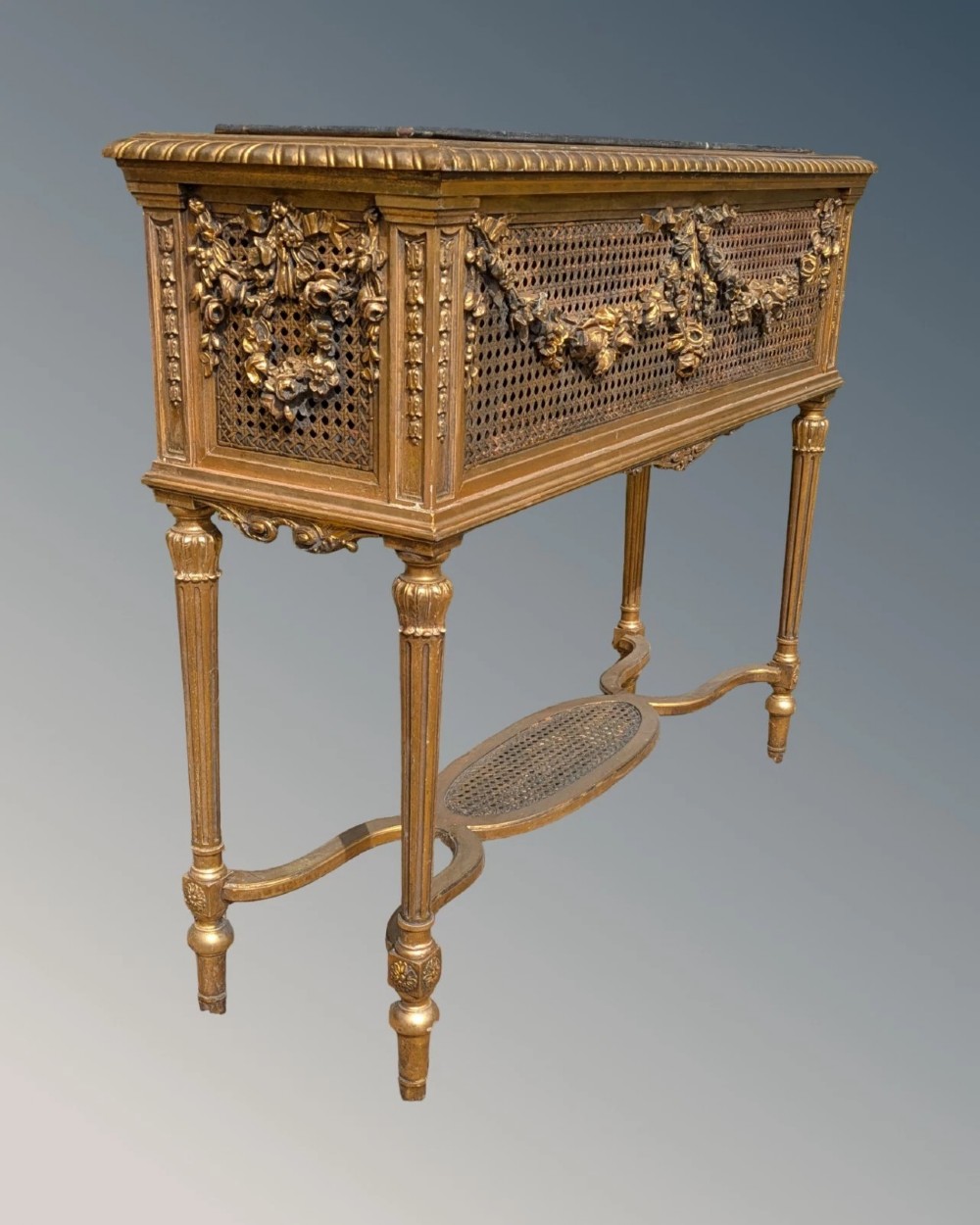 An antique Louis XVI style giltwood and cane jardiniere stand featuring carved floral swags, fluted legs, and an oval stretcher. View IV