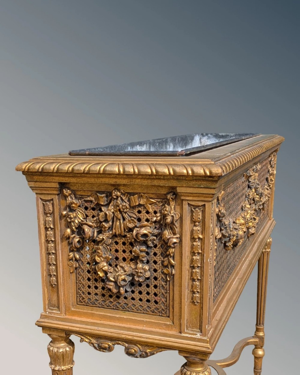 An antique Louis XVI style giltwood and cane jardiniere stand featuring carved floral swags, fluted legs, and an oval stretcher. View V