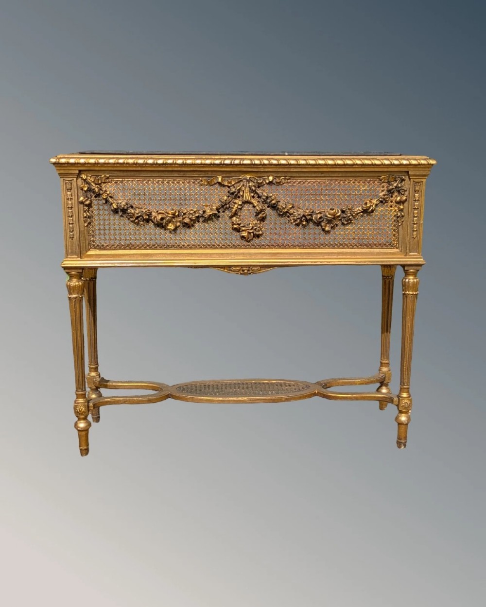 An antique Louis XVI style giltwood and cane jardiniere stand featuring carved floral swags, fluted legs, and an oval stretcher. View VII