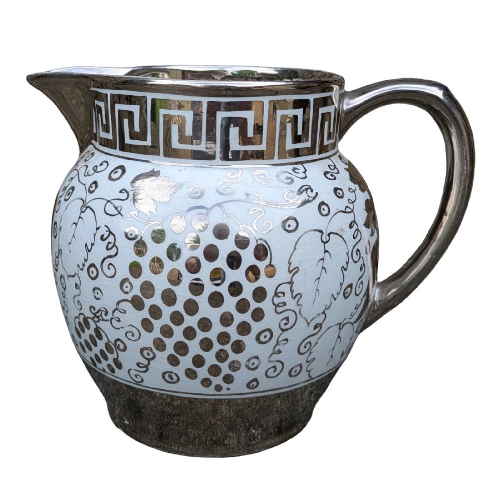 A white pearlware ceramic jug with silver lustre trim, featuring a Greek key band along the neck and a grape and vine pattern around the body.