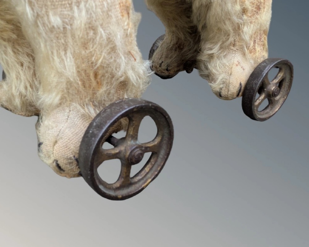 An early twentieth-century off-white mohair Steiff bear standing quadrupedally on four metal wheels. View IV