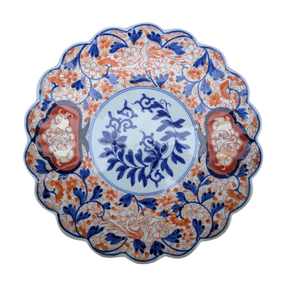 A circular Japanese Imari porcelain charger featuring a scalloped rim, hand-painted cobalt blue and iron red floral patterns, and a central botanical roundel.