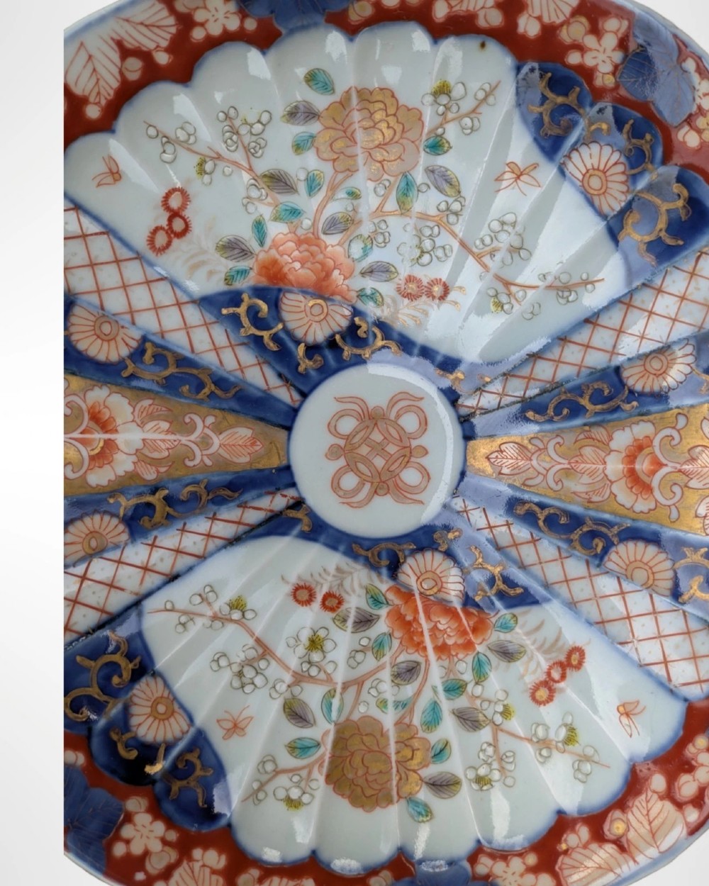 A circular Japanese Imari porcelain plate featuring a scalloped rim, fluted surface, and floral motifs in cobalt blue, iron red, and gold decoration. View III
