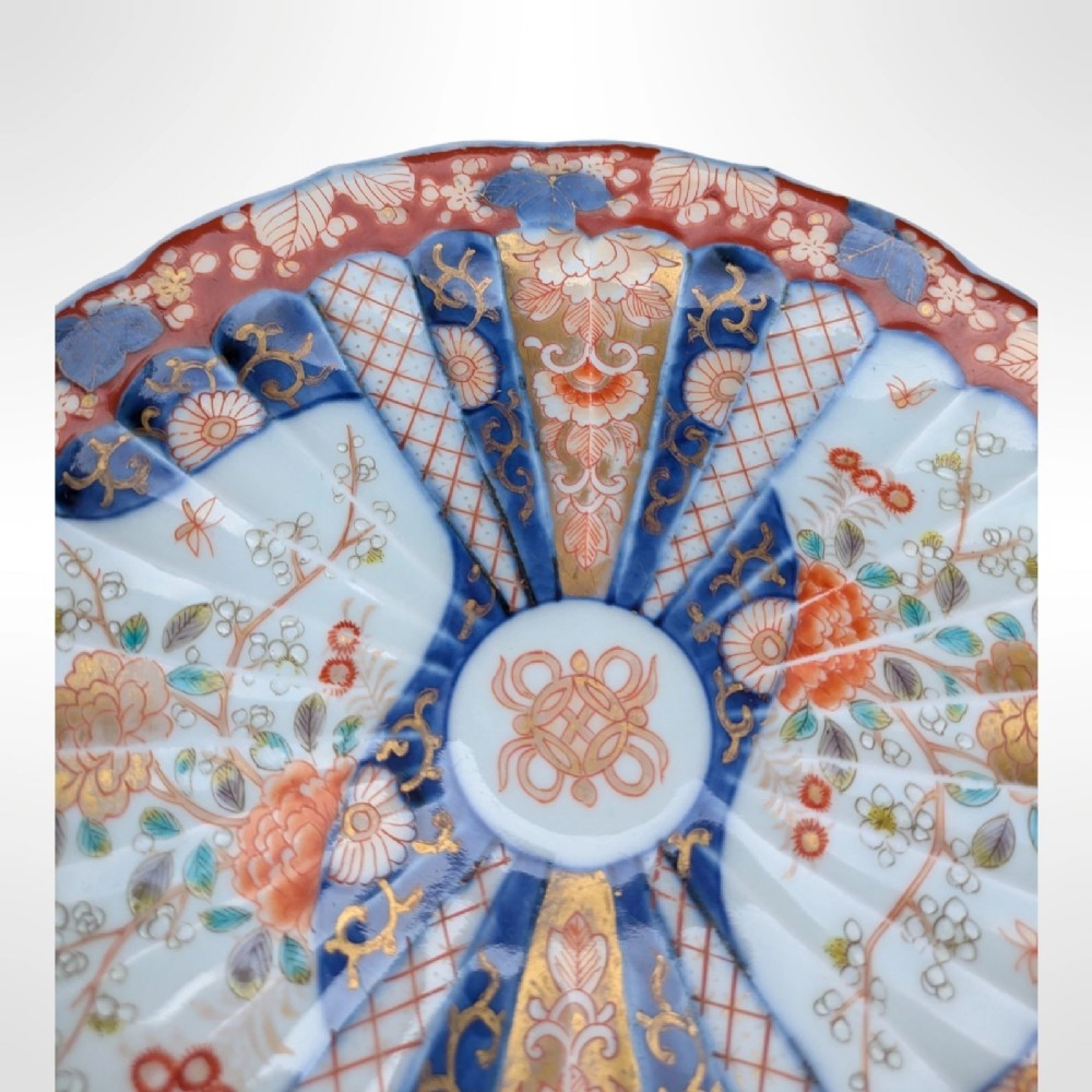 A circular Japanese Imari porcelain plate featuring a scalloped rim, fluted surface, and floral motifs in cobalt blue, iron red, and gold decoration. View IV