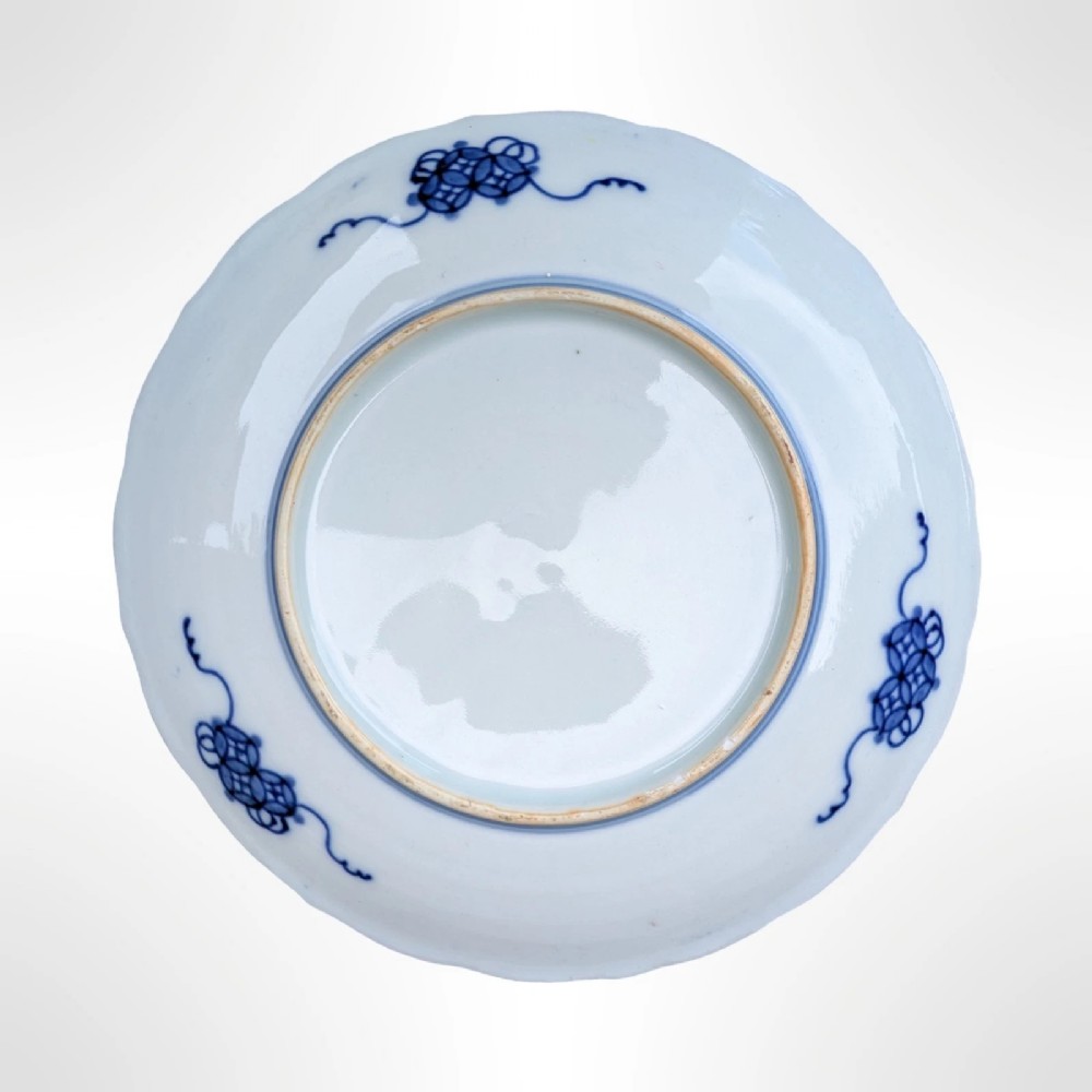 A circular Japanese Imari porcelain plate featuring a scalloped rim, fluted surface, and floral motifs in cobalt blue, iron red, and gold decoration. View V
