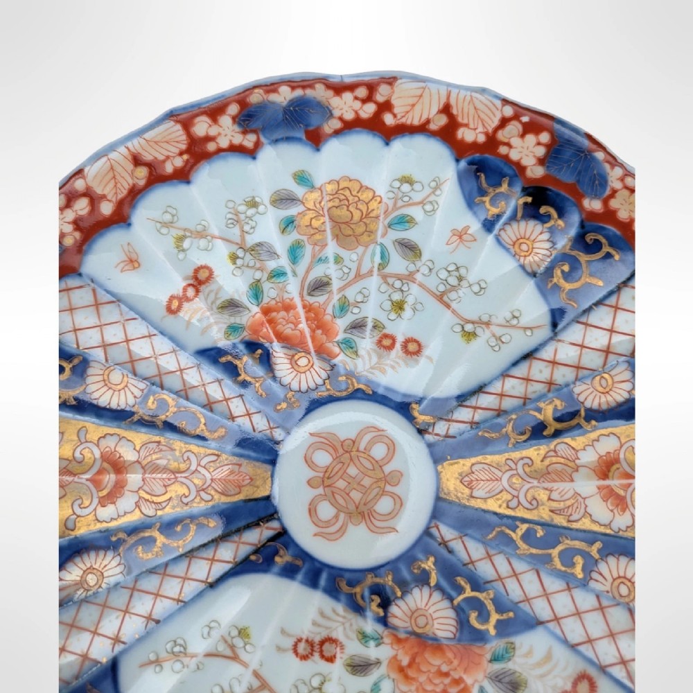 A circular Japanese Imari porcelain plate featuring a scalloped rim, fluted surface, and floral motifs in cobalt blue, iron red, and gold decoration. View VI