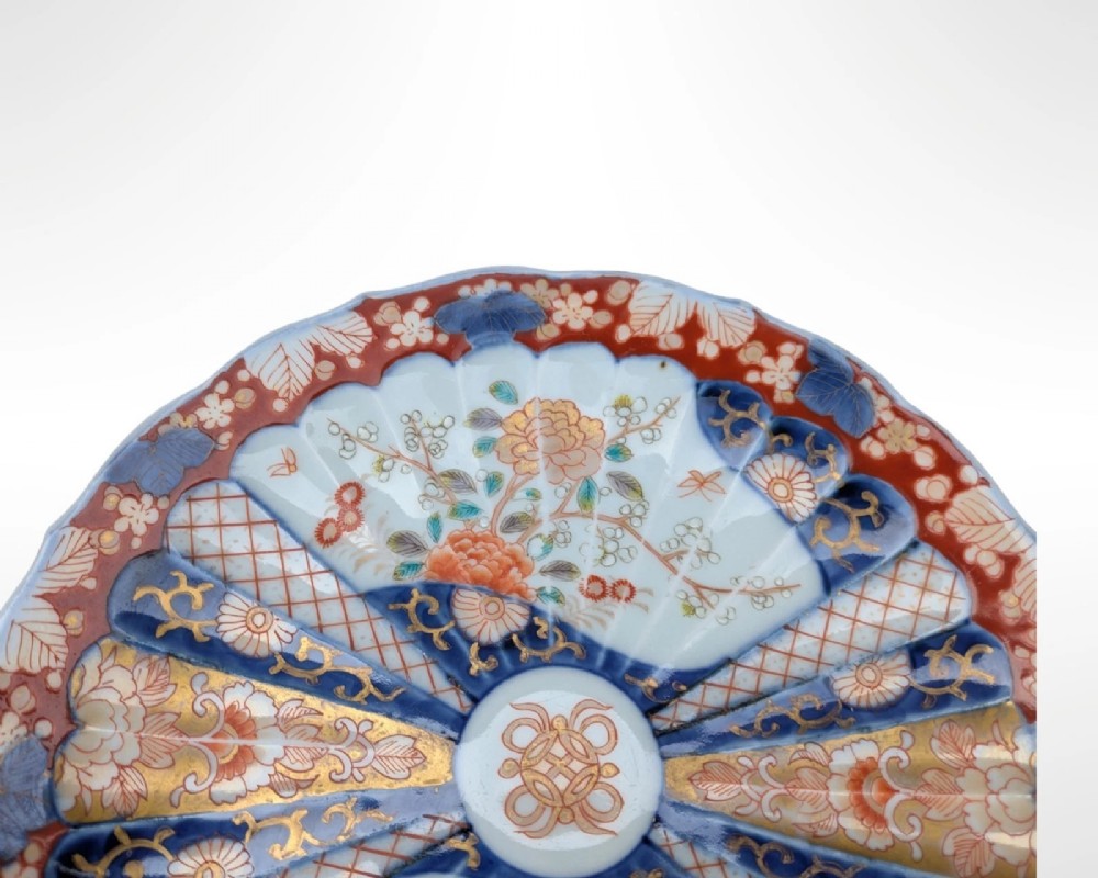 A circular Japanese Imari porcelain plate featuring a scalloped rim, fluted surface, and floral motifs in cobalt blue, iron red, and gold decoration. View VII
