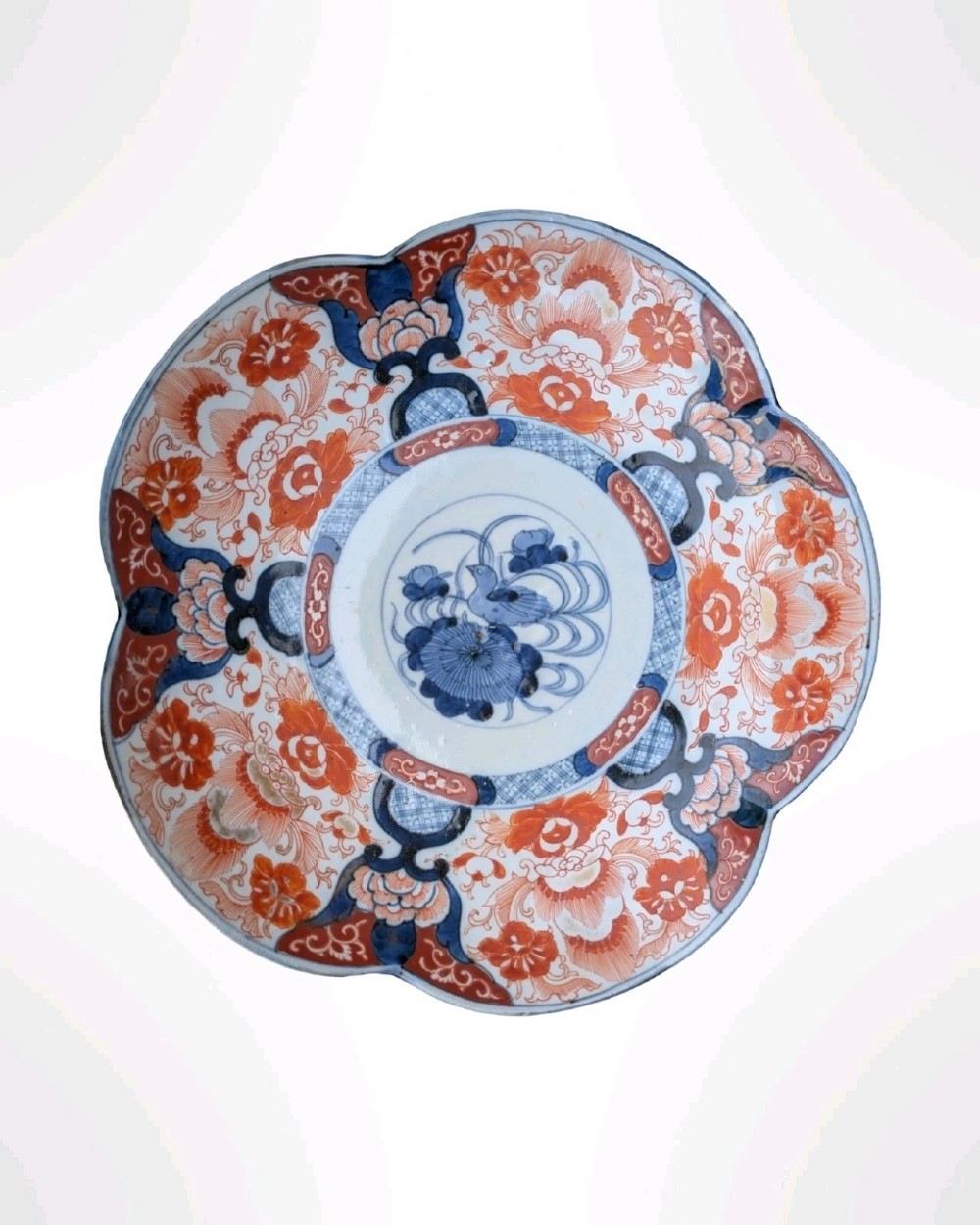 A lobed Japanese Imari porcelain dish featuring red floral patterns, blue underglaze details, and a central circular medallion depicting a bird.