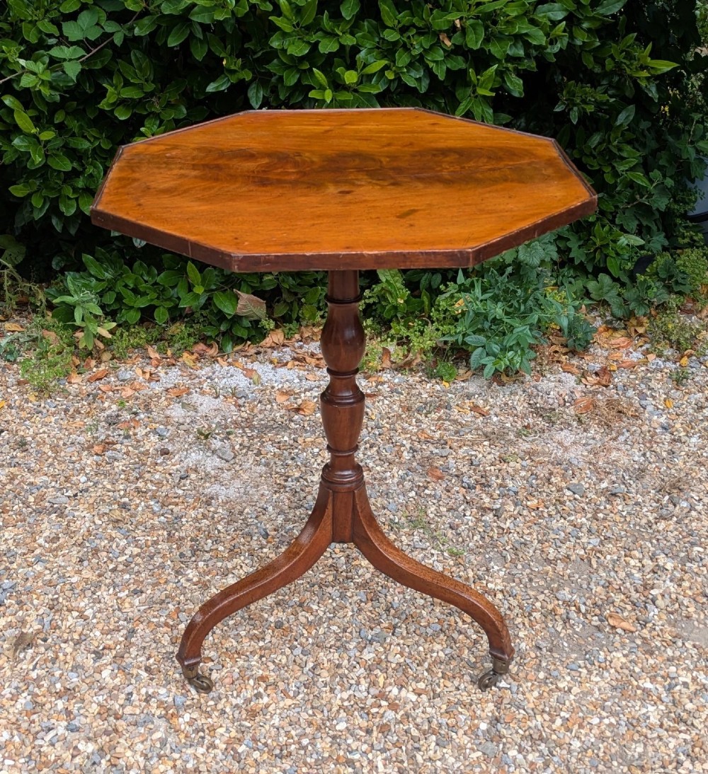 An antique Regency mahogany occasional table featuring an octagonal tilt-top surface, a turned central pedestal stem, three splayed tripod legs, and brass castors. View III