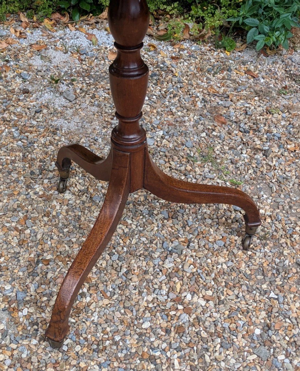 An antique Regency mahogany occasional table featuring an octagonal tilt-top surface, a turned central pedestal stem, three splayed tripod legs, and brass castors. View IV
