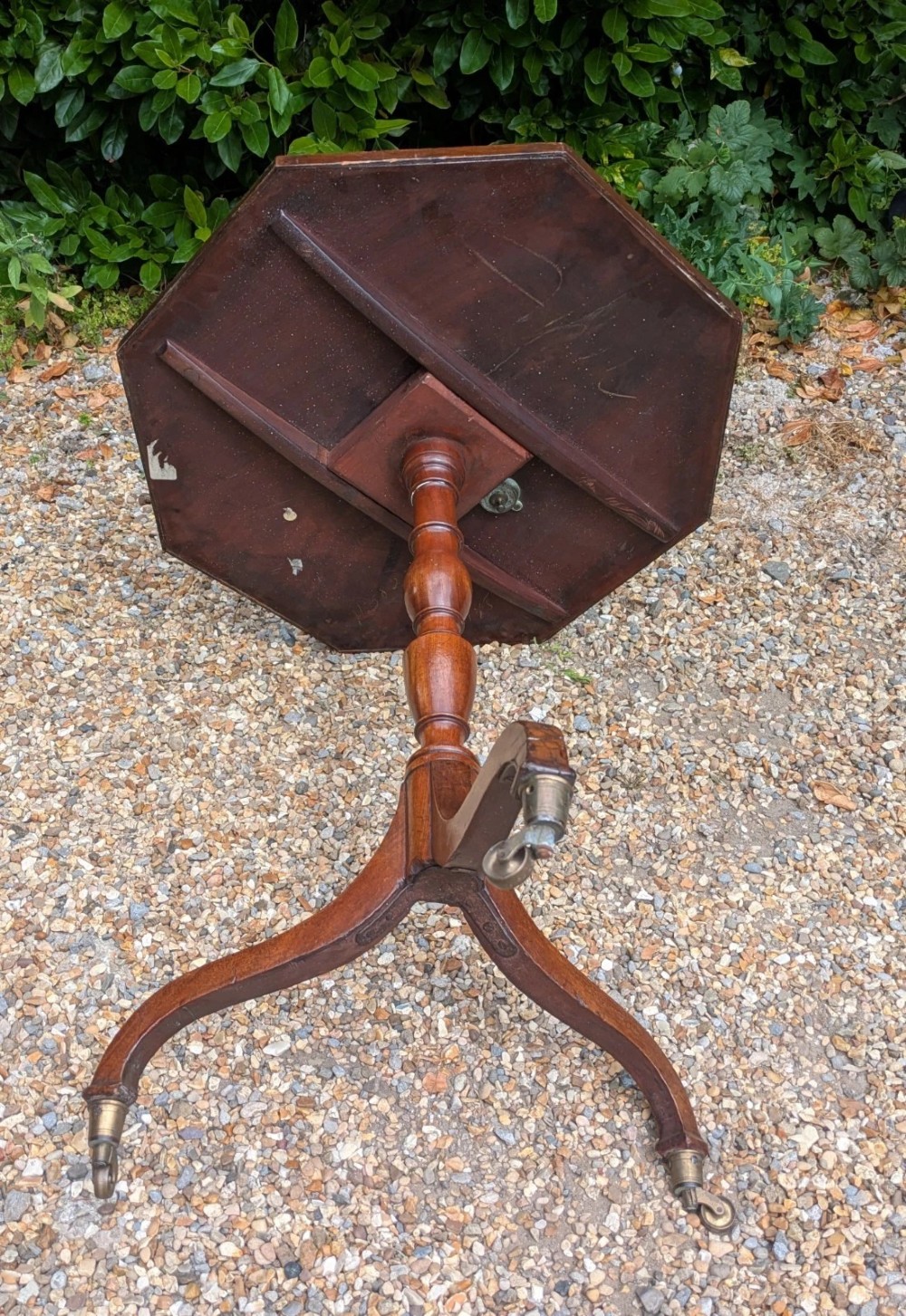 An antique Regency mahogany occasional table featuring an octagonal tilt-top surface, a turned central pedestal stem, three splayed tripod legs, and brass castors. View VI