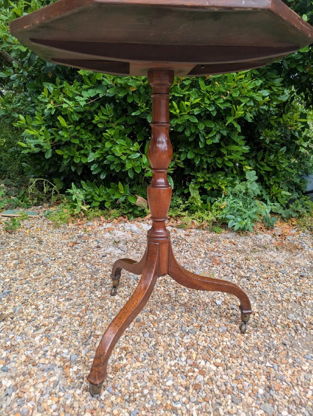 An antique Regency mahogany occasional table featuring an octagonal tilt-top surface, a turned central pedestal stem, three splayed tripod legs, and brass castors. View VII