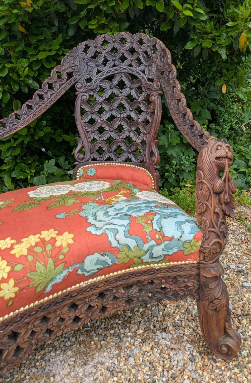 An antique Anglo-Indian carved hardwood sofa featuring an ornate openwork pierced backrest, carved lion armrests, and a patterned coral upholstered seat. View III