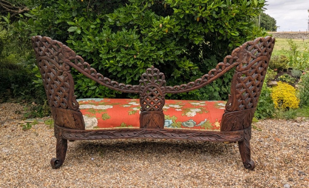 An antique Anglo-Indian carved hardwood sofa featuring an ornate openwork pierced backrest, carved lion armrests, and a patterned coral upholstered seat. View VIII