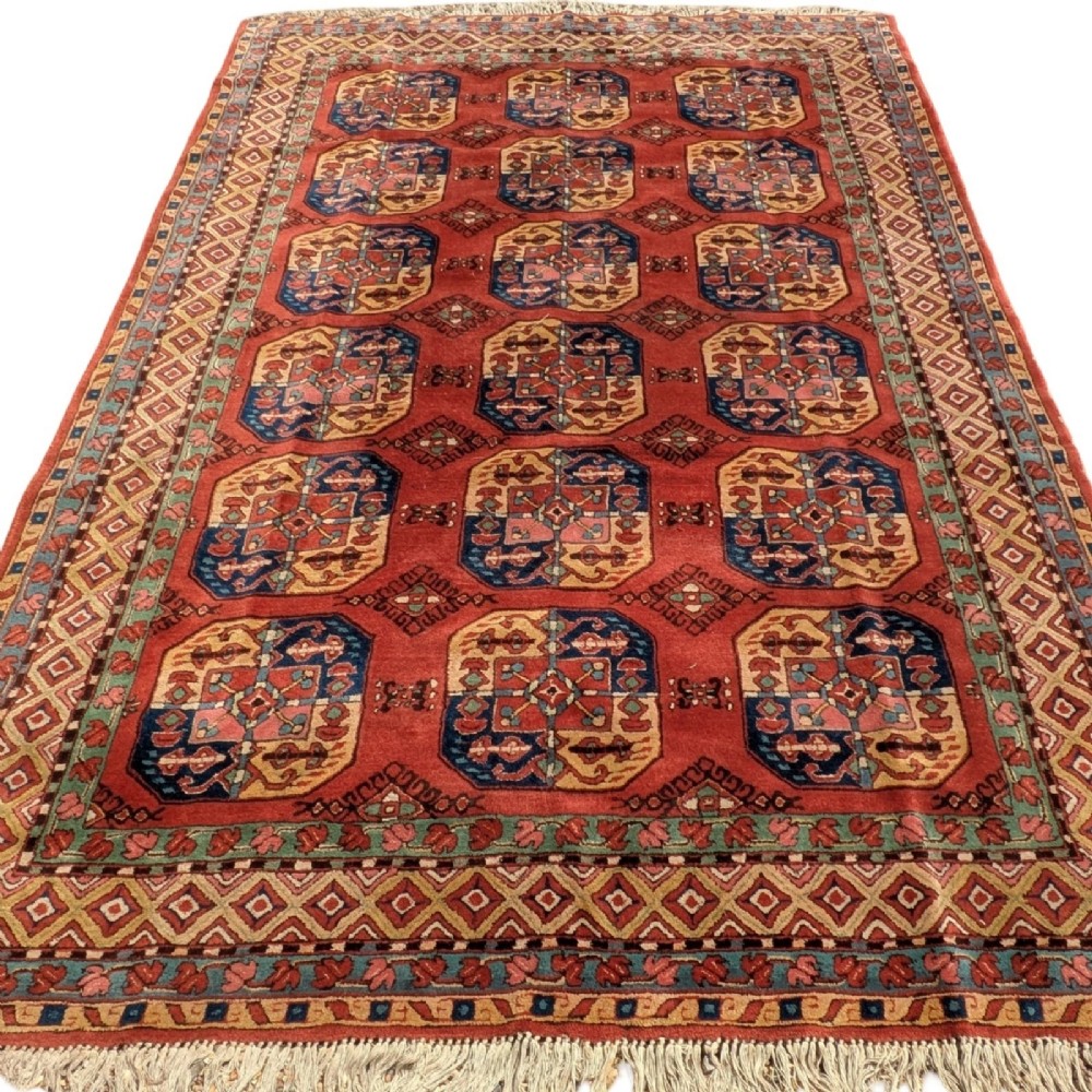 A hand-knotted rectangular wool carpet featuring repeating octagonal tribal gul motifs on a deep red field framed by geometric borders. View II