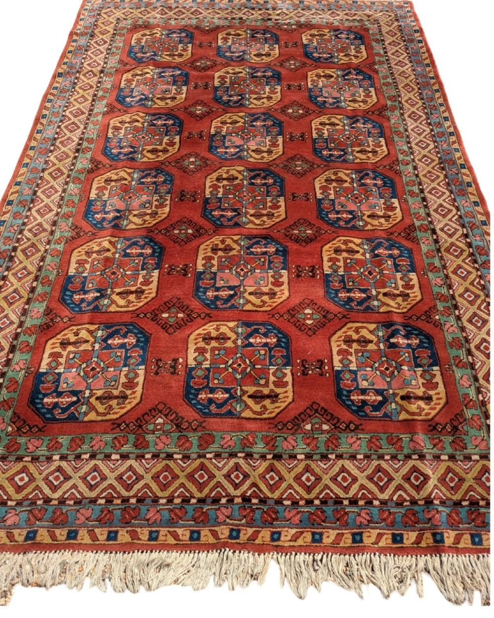 A hand-knotted rectangular wool carpet featuring repeating octagonal tribal gul motifs on a deep red field framed by geometric borders. View III