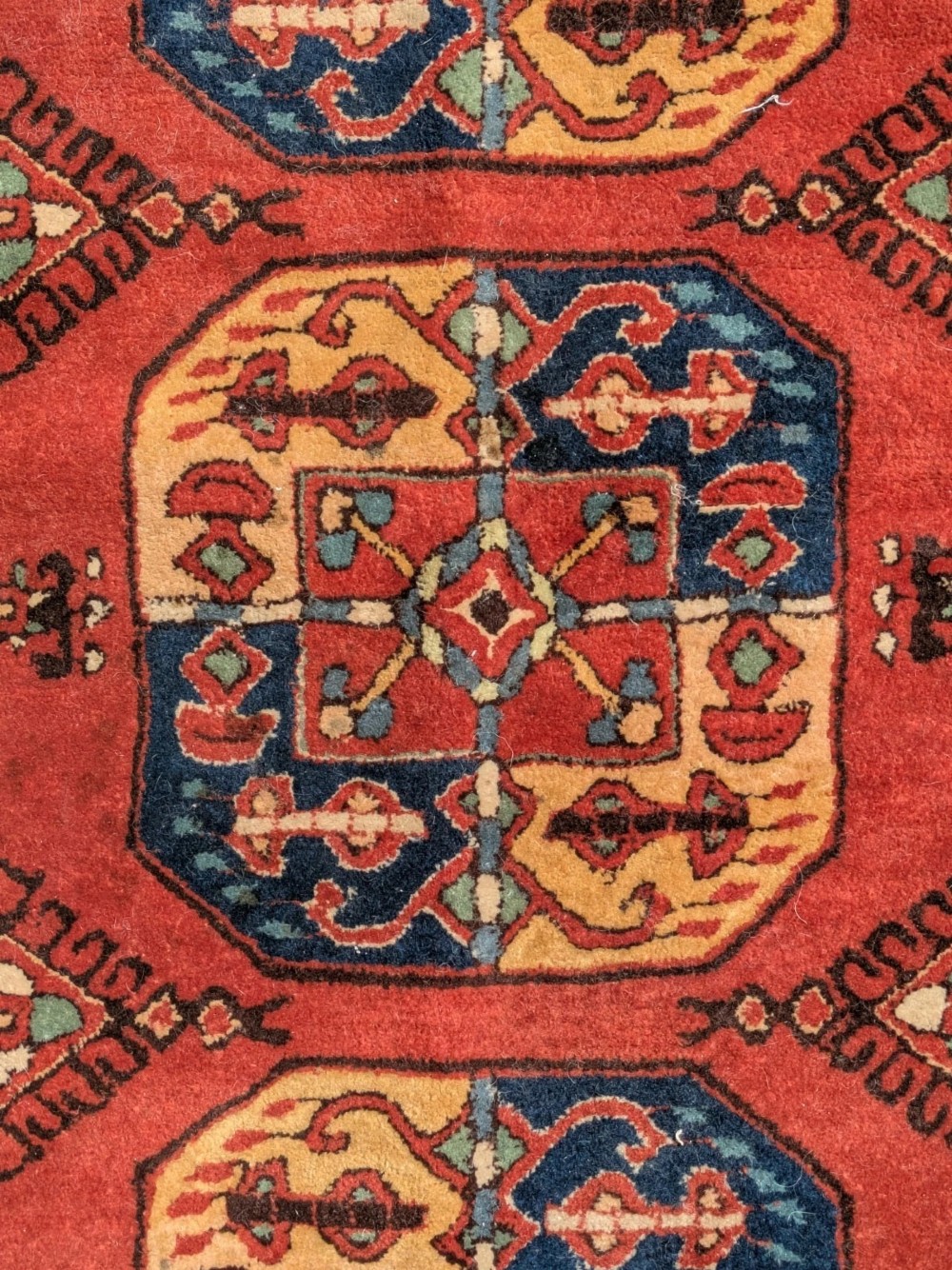 A hand-knotted rectangular wool carpet featuring repeating octagonal tribal gul motifs on a deep red field framed by geometric borders. View V