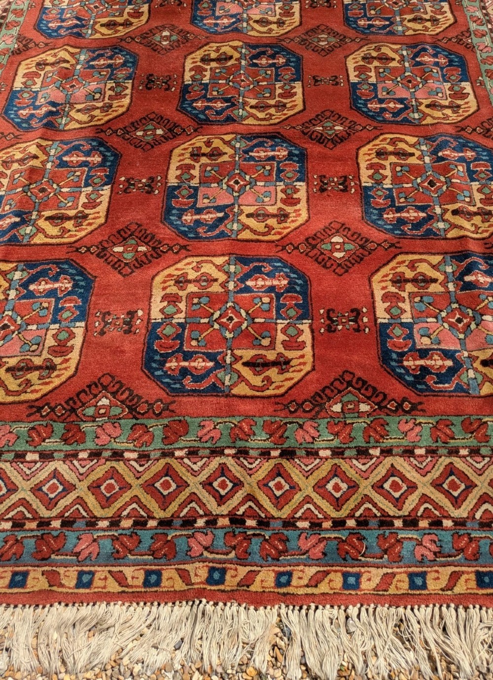A hand-knotted rectangular wool carpet featuring repeating octagonal tribal gul motifs on a deep red field framed by geometric borders. View VII