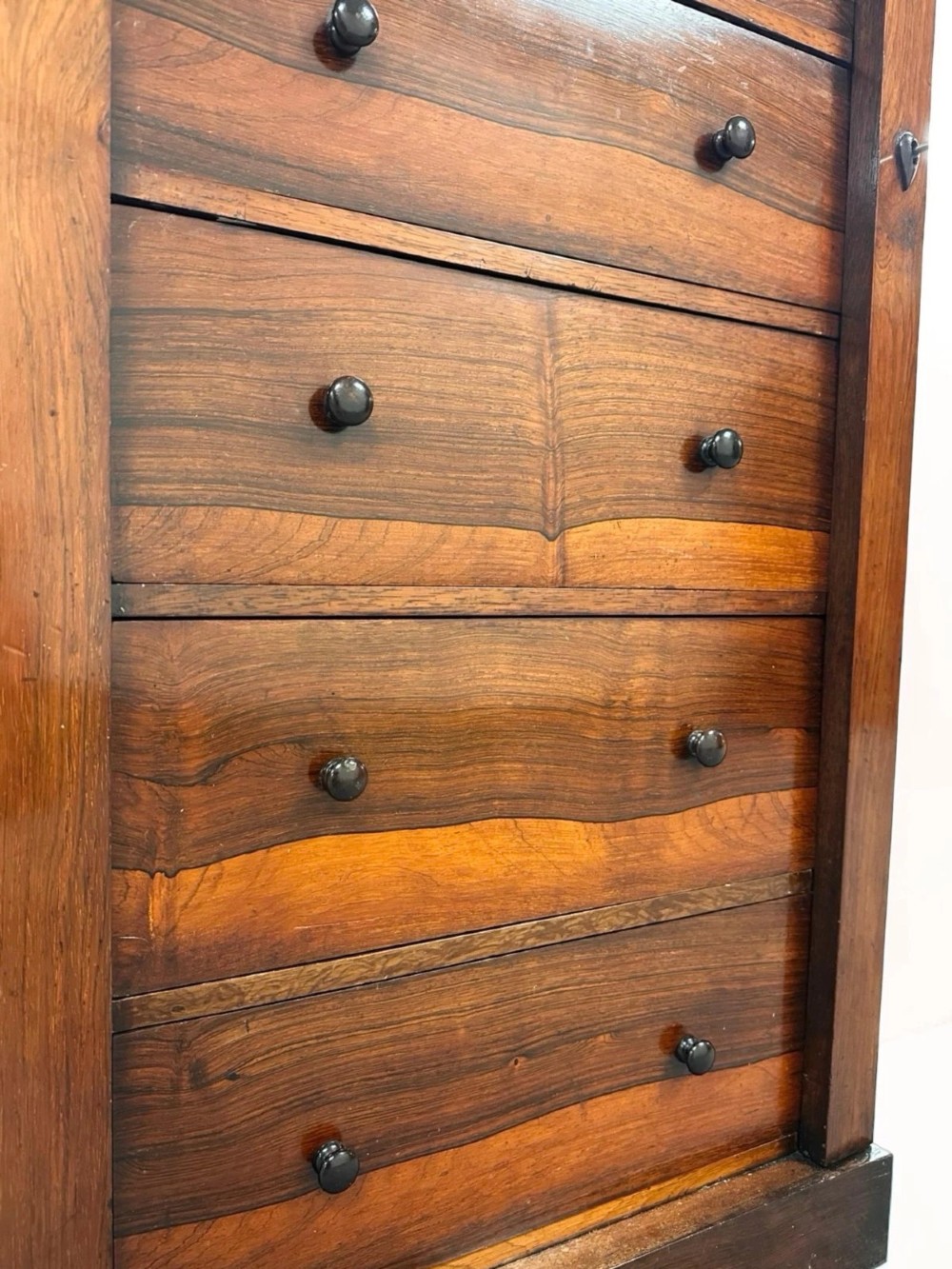 An antique Victorian rosewood Wellington chest featuring seven stacked drawers, turned wooden knobs, carved upper corbels, and a side locking bar. View V