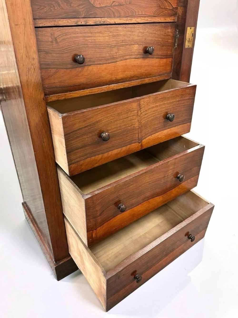 An antique Victorian rosewood Wellington chest featuring seven stacked drawers, turned wooden knobs, carved upper corbels, and a side locking bar. View VII