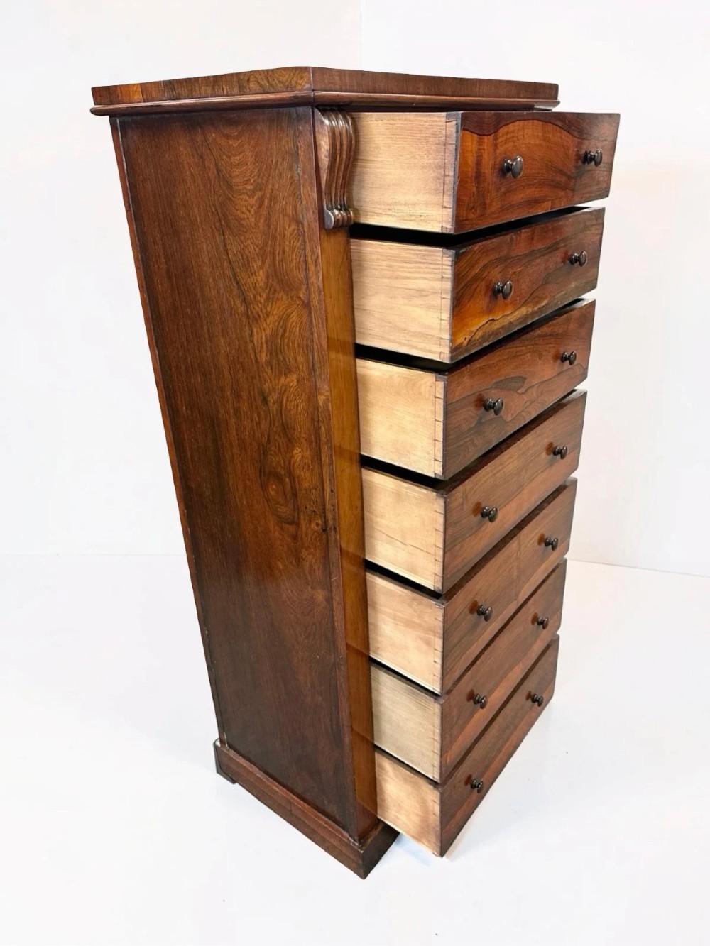 An antique Victorian rosewood Wellington chest featuring seven stacked drawers, turned wooden knobs, carved upper corbels, and a side locking bar. View VIII
