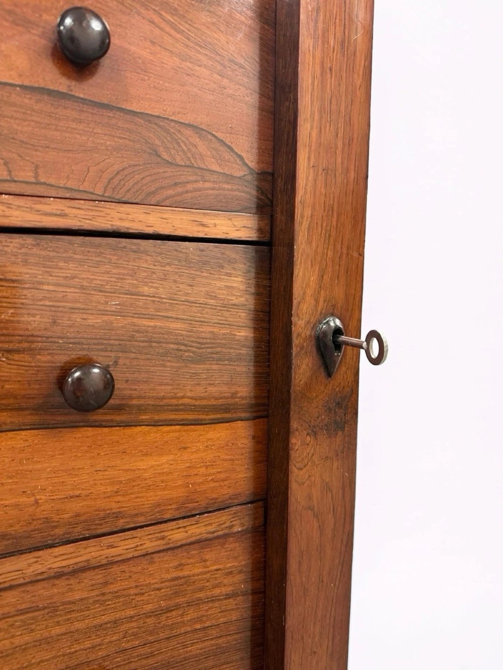 An antique Victorian rosewood Wellington chest featuring seven stacked drawers, turned wooden knobs, carved upper corbels, and a side locking bar. View IX