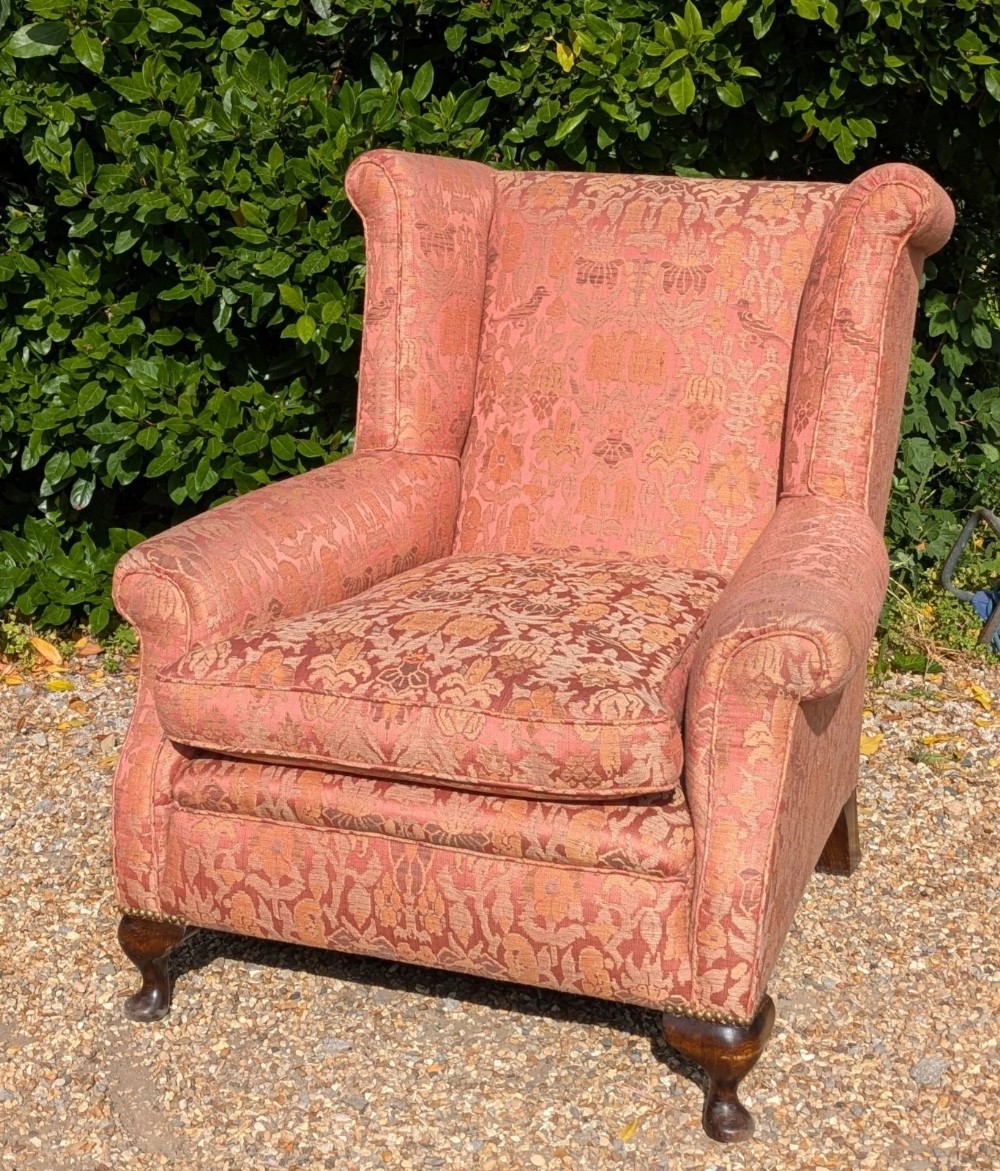 An upholstered wingback armchair in terracotta patterned damask fabric with a feather-filled seat cushion and carved timber cabriole legs.