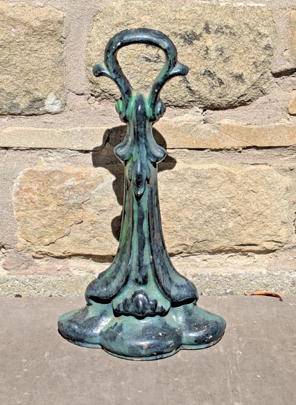 An Art Nouveau cast iron doorstop featuring a vertical stem with organic leaf motifs, a loop handle at the top, and a green patinated finish. View III