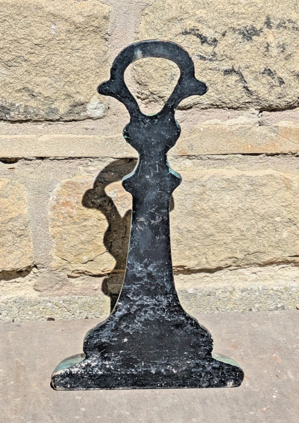 An Art Nouveau cast iron doorstop featuring a vertical stem with organic leaf motifs, a loop handle at the top, and a green patinated finish. View VI