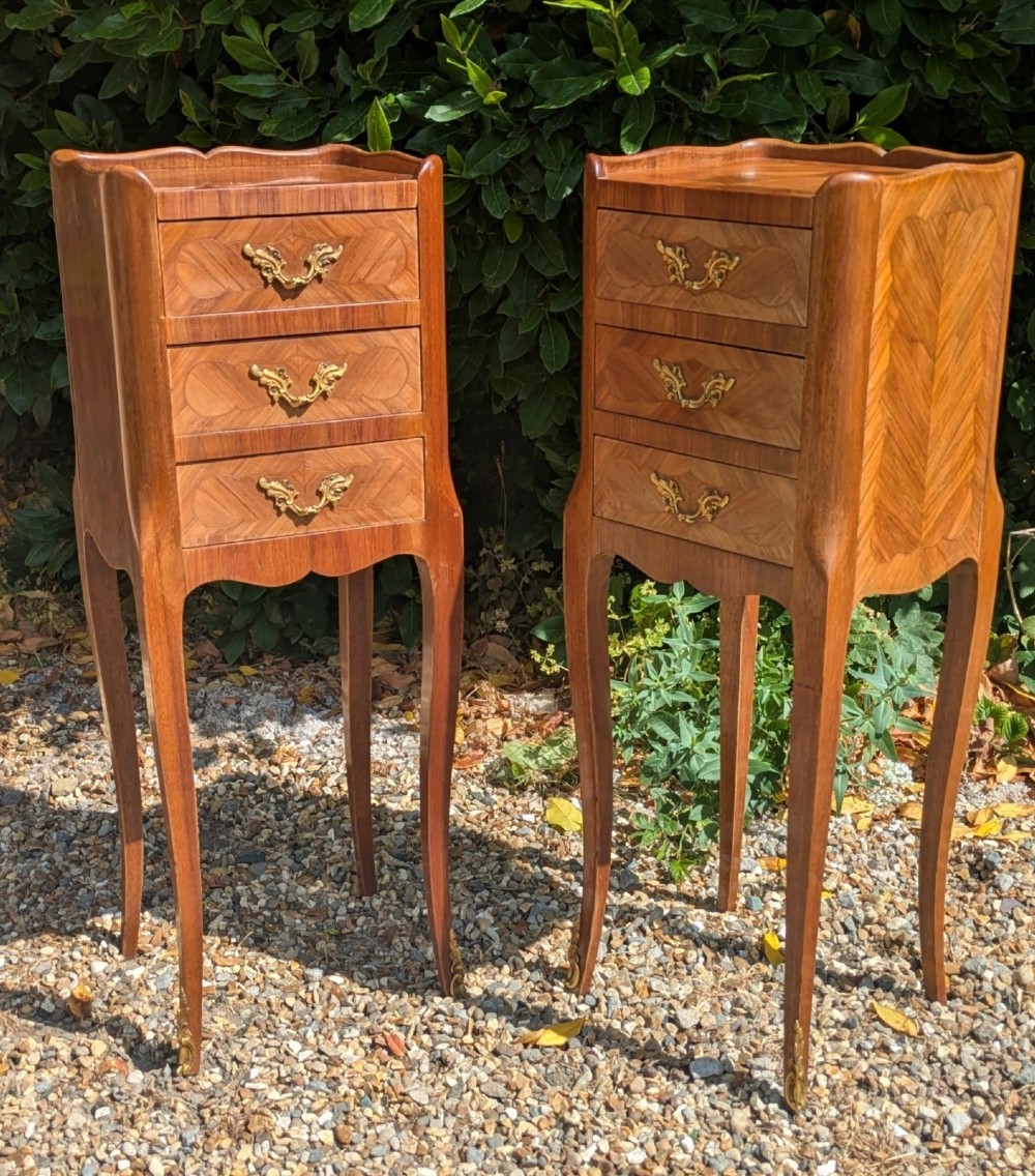 A pair of tall, slim French Louis XV style bedside cabinets crafted with geometric wood parquetry, featuring three drawers with ornate gilt handles and long cabriole legs with metal sabots. View II