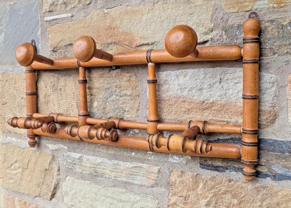 A wall-mounted wooden coat rack crafted with faux bamboo turned timber detailing and multiple spherical and lathe-turned hanging pegs.