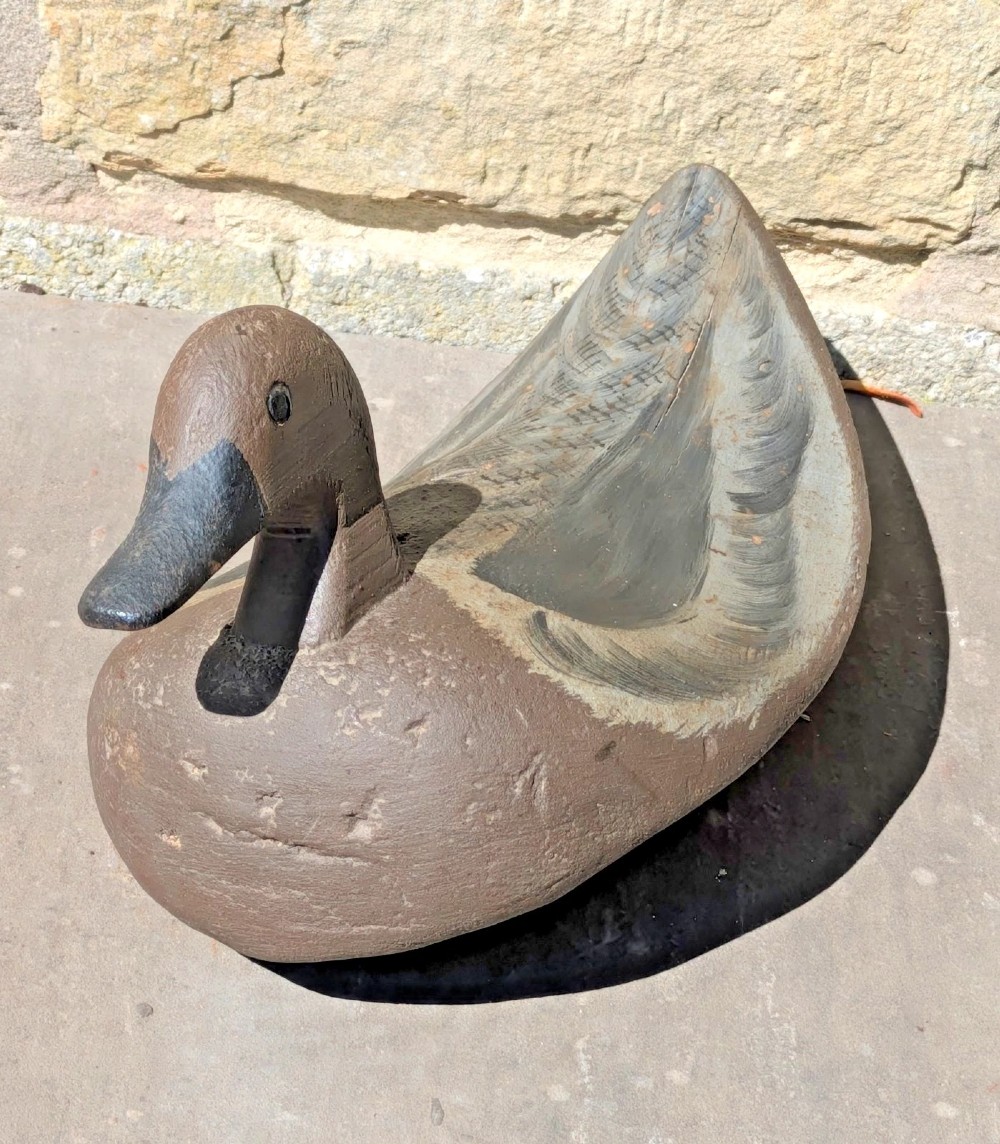 A hand-carved wooden decoy duck painted in earthy brown and grey tones with subtle feather detailing.
