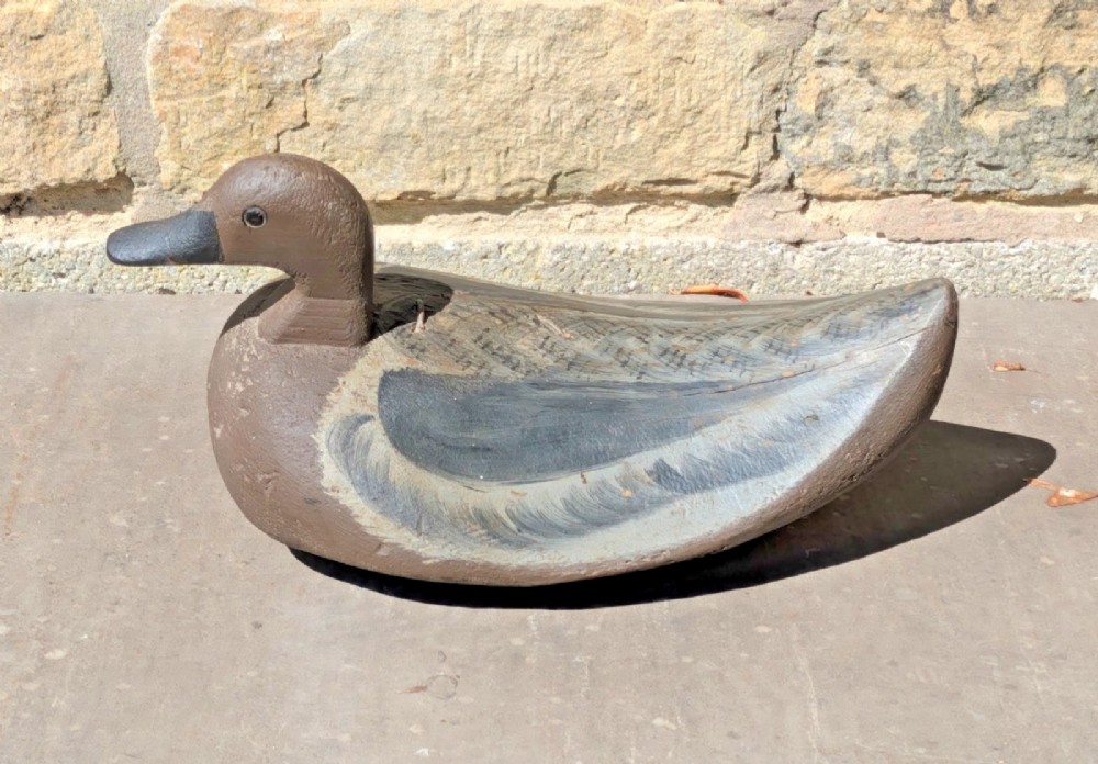 A hand-carved wooden decoy duck painted in earthy brown and grey tones with subtle feather detailing. View IV