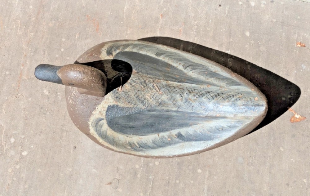 A hand-carved wooden decoy duck painted in earthy brown and grey tones with subtle feather detailing. View VI
