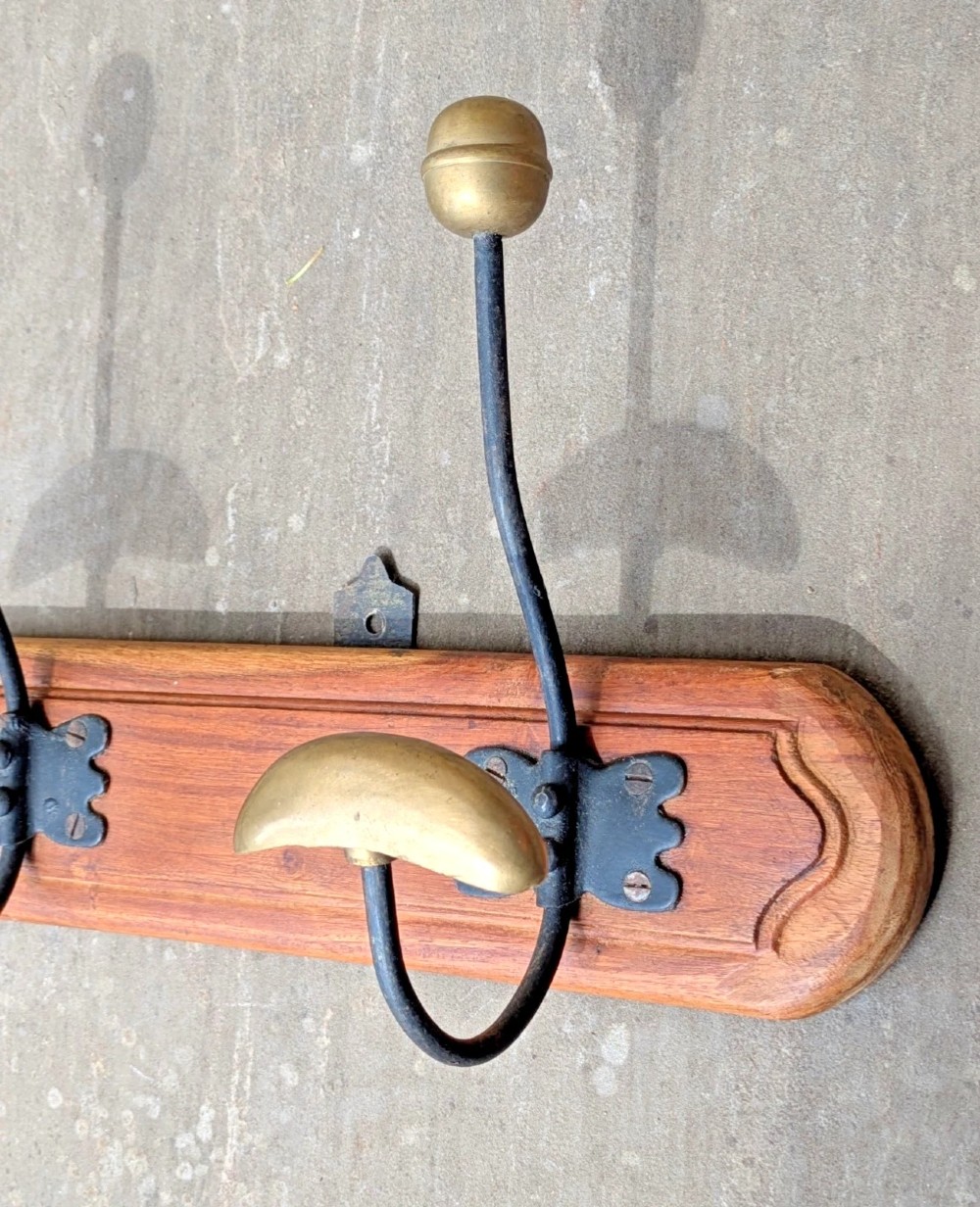 An antique French wall coat rack featuring a moulded wooden board with three brass and iron coat and hat hooks. View II