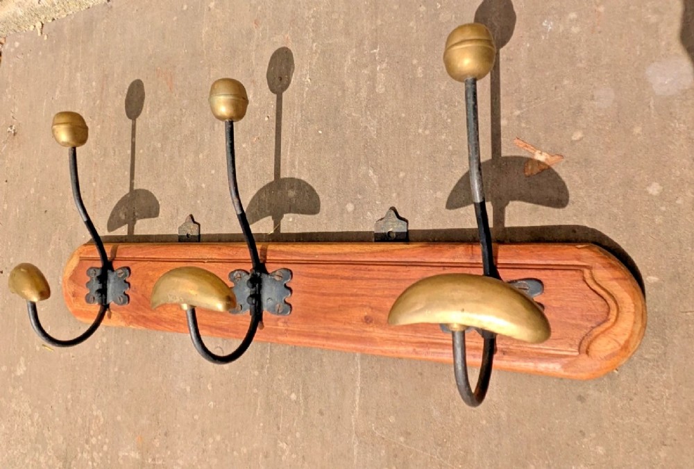 An antique French wall coat rack featuring a moulded wooden board with three brass and iron coat and hat hooks. View V