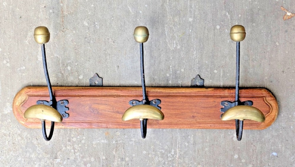 An antique French wall coat rack featuring a moulded wooden board with three brass and iron coat and hat hooks. View VI