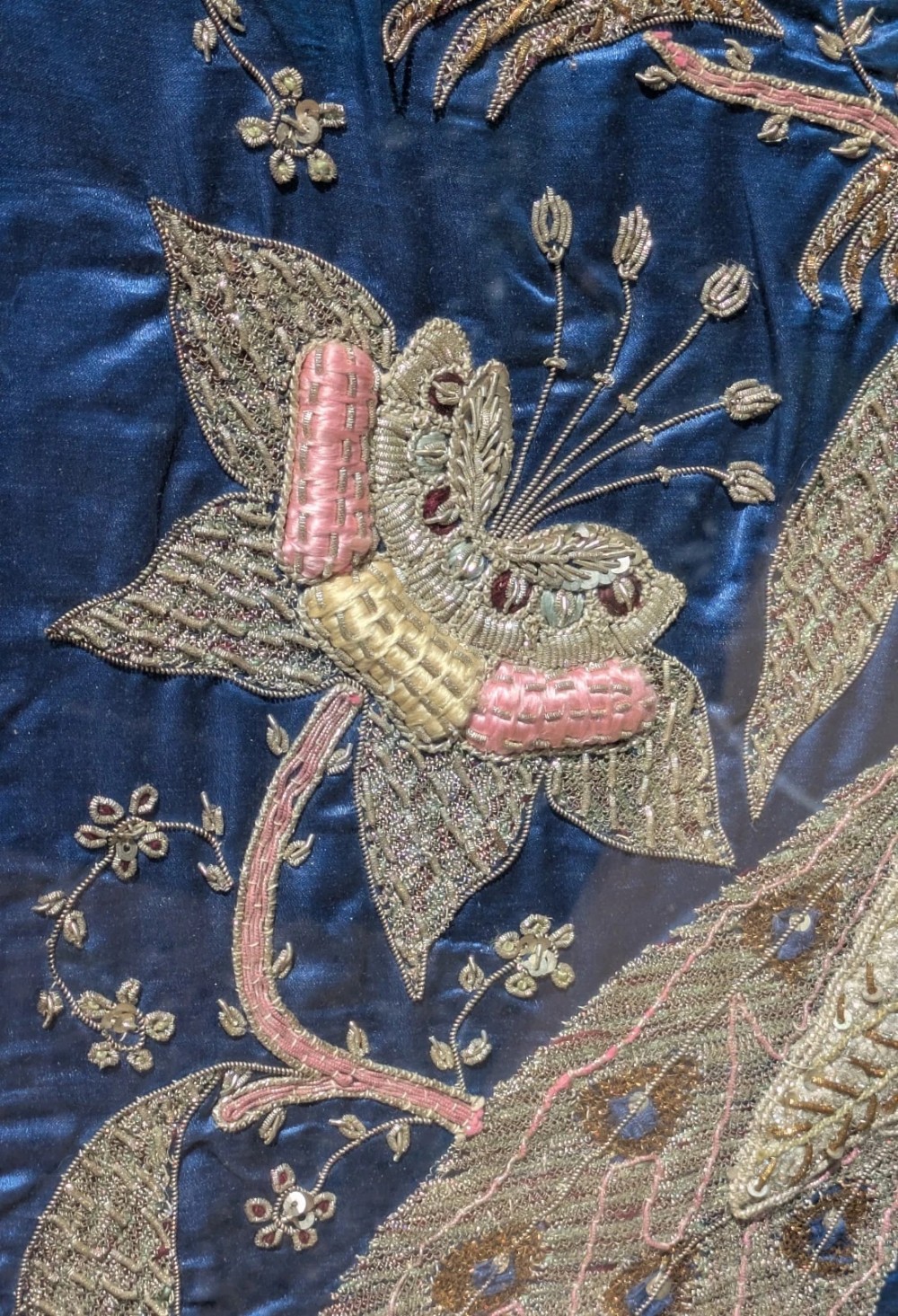 A framed vertical silk textile panel displaying metallic thread zardozi embroidery of peacocks, flowers, and the Taj Mahal on a cobalt blue ground. View V