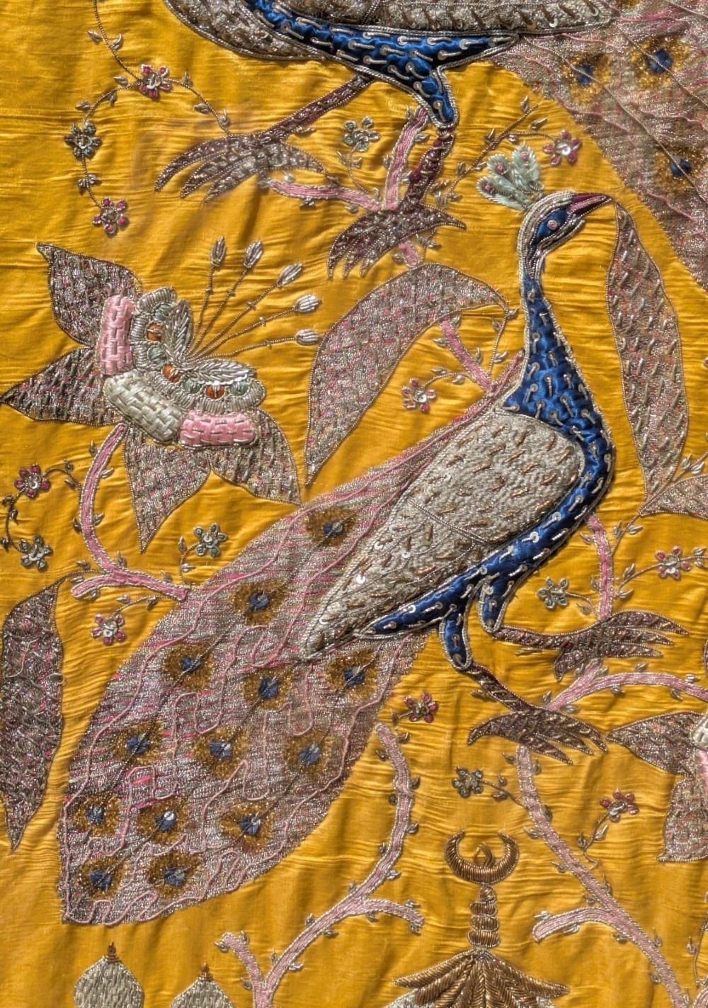 Framed vertical yellow silk panel embroidered with two peacocks, floral motifs, and an architectural depiction of the Taj Mahal in metallic thread. View VI