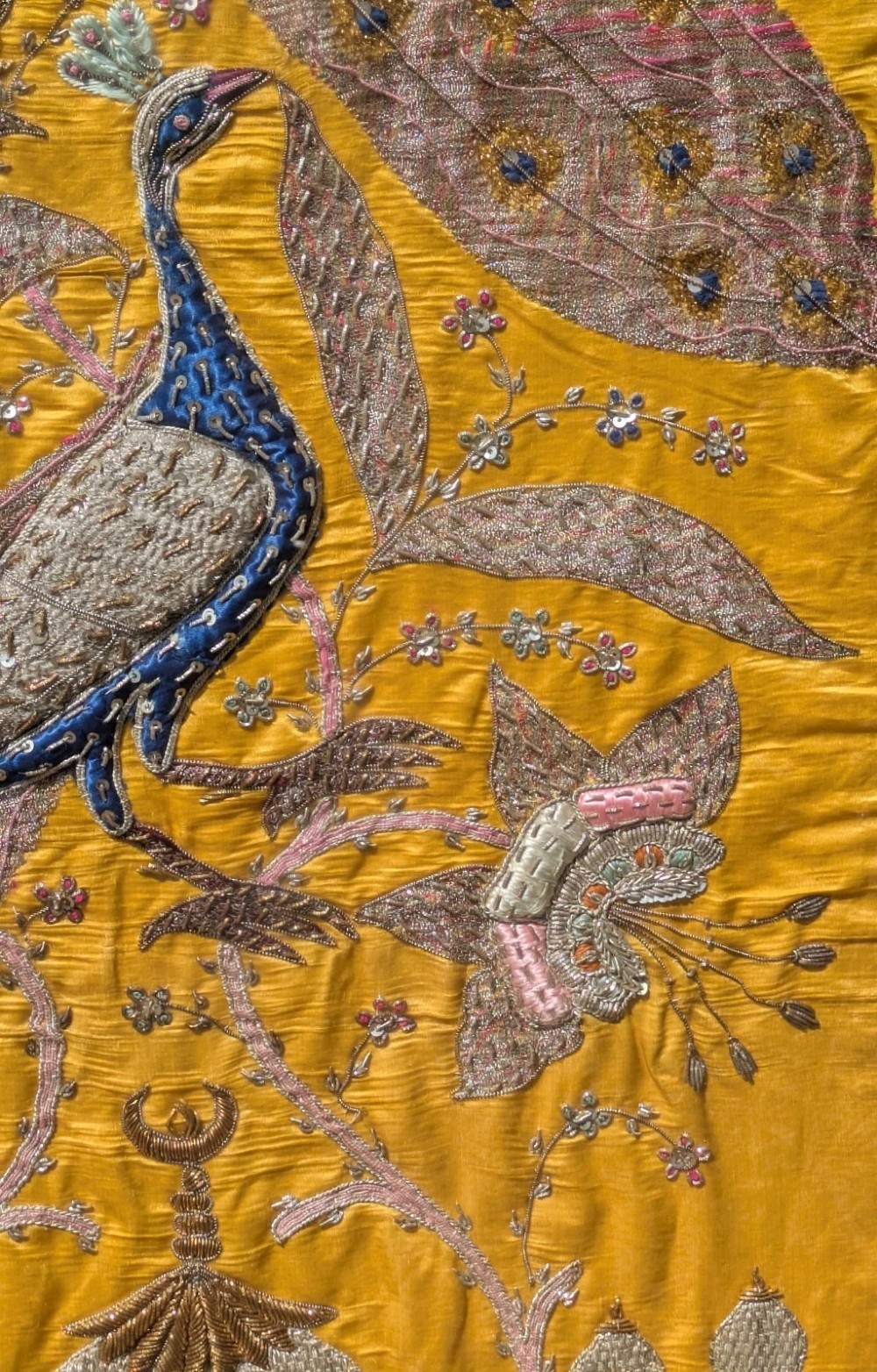 Framed vertical yellow silk panel embroidered with two peacocks, floral motifs, and an architectural depiction of the Taj Mahal in metallic thread. View VIII