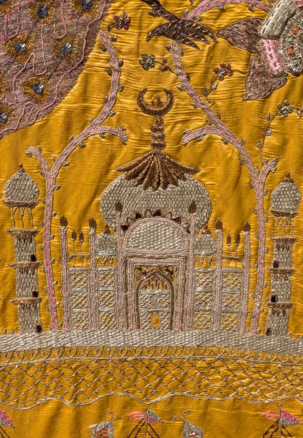 Framed vertical yellow silk panel embroidered with two peacocks, floral motifs, and an architectural depiction of the Taj Mahal in metallic thread. View X